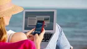 Una mujer con su móvil y su portátil en la playa