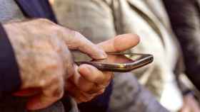 Un hombre anciano pulsa la pantalla de un teléfono móvil con su dedo