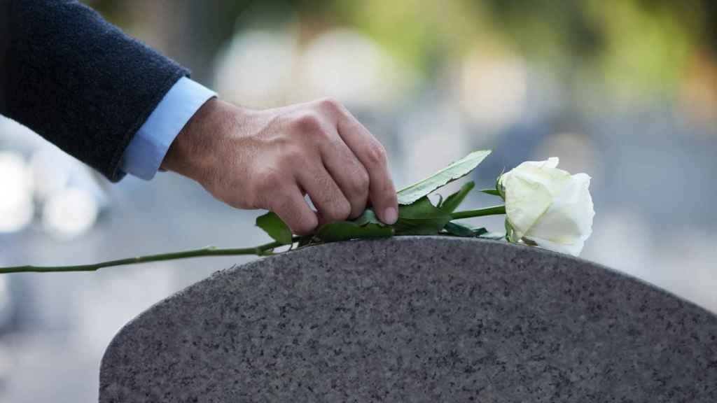 Un hombre deposita una flor en una tumba.