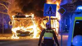 Un agente delante de autobús que arde en medio de los disturbios en Malmö.