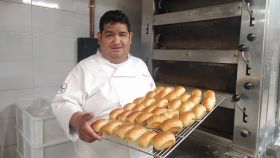 John Torres, sujetando un bandeja de panes delante del horno de su obrador.