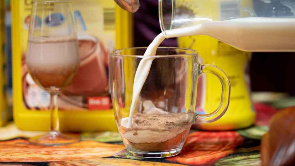 Helen López echa tres cucharaditas de cacao soluble en una taza y le añade leche entera.