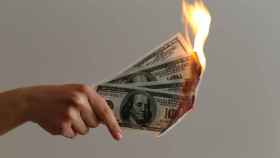 Una mujer quema varios billetes de cien dólares.