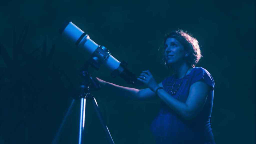Una mujer embarazada observa el cielo con su telescopio.