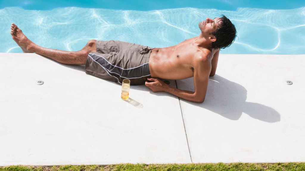 Un hombre toma el sol en el borde de una piscina.