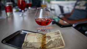 Un billete de 100 pesetas junto a una copa en la barra de un bar.