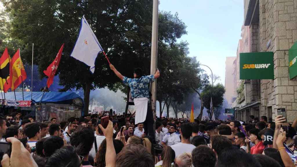 Un aficionado madridista, sobre una farola, ondeando una bandera del Real Madrid.
