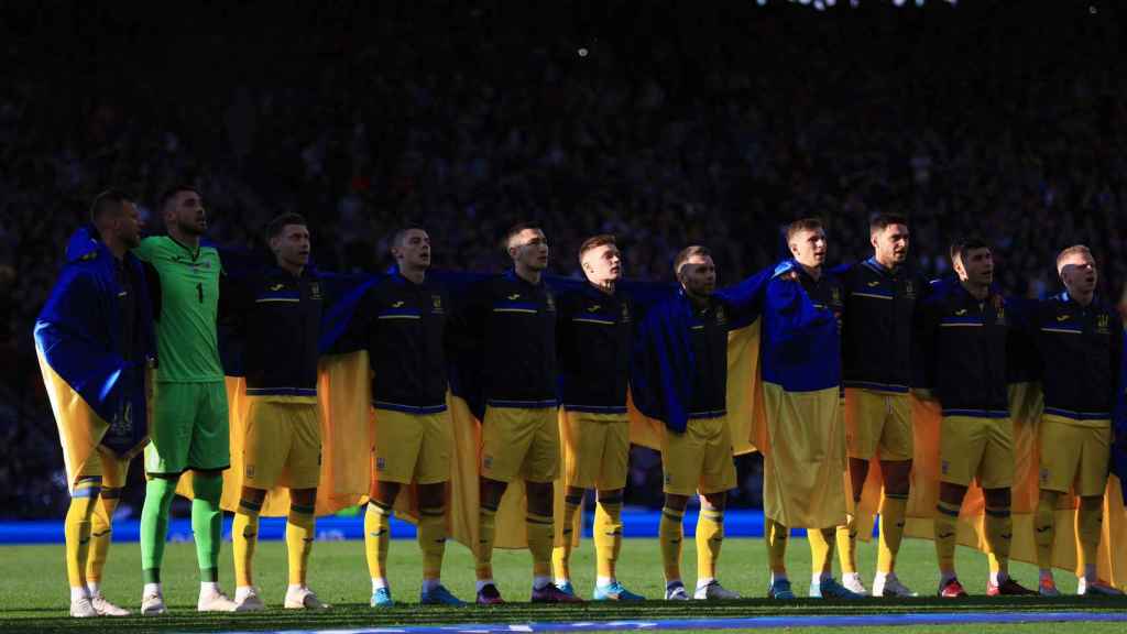 Los jugadores de la selección de Ucrania, escuchando el himno con su bandera sobre los hombros