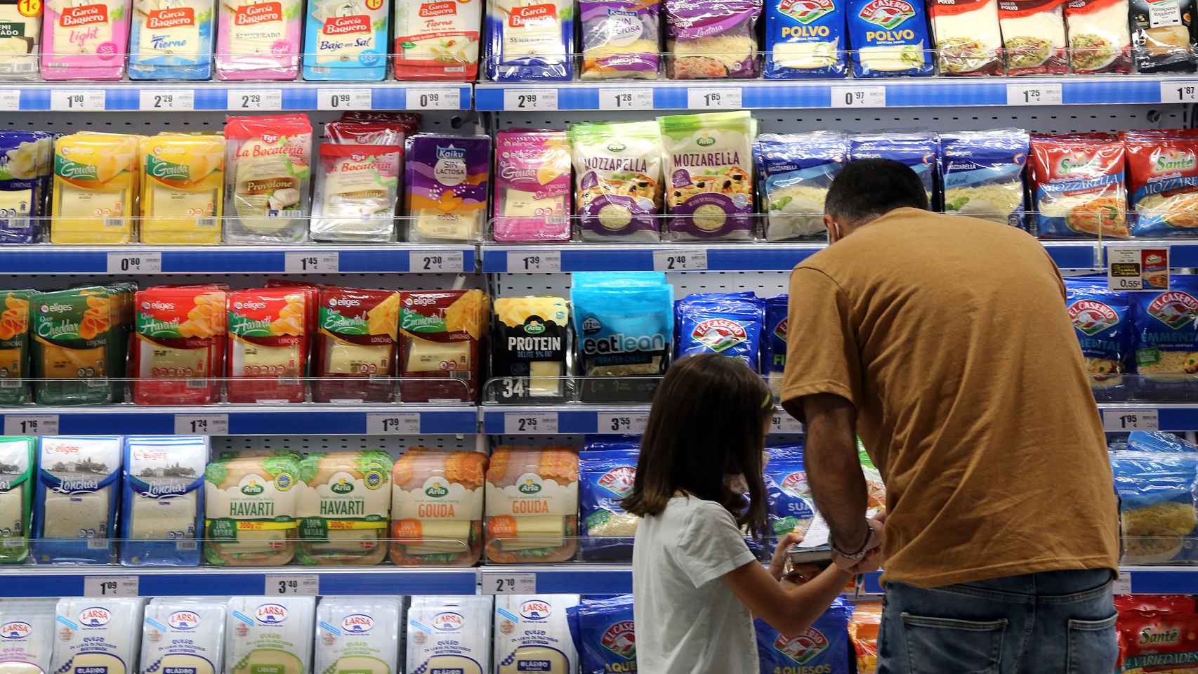 Un padre mira los precios de los alimentos en un lineal de un supermercado.