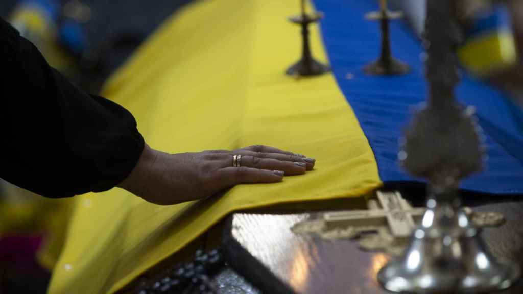 Una persona toca la bandera ucraniana sobre el féretro de un soldado ucraniano.