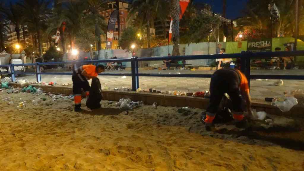 Dos operarios limpian una playa de Alicante tras la noche de San Juan.