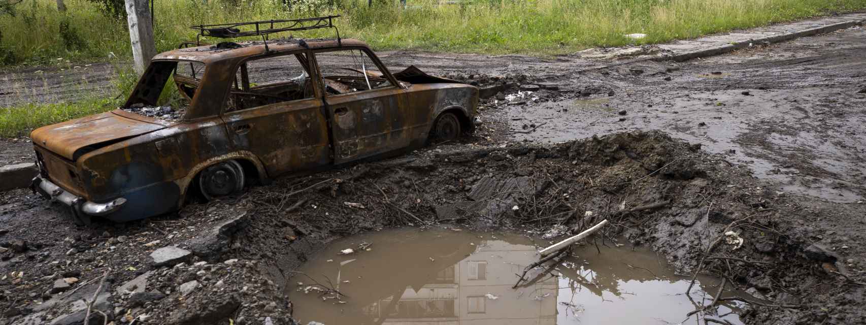 Fotografía de un automóvil destruido junto al cráter dejado por una explosión en la entrada del barrio Saltivka, este sábado 25 de junio en Jarkov (Ucrania).