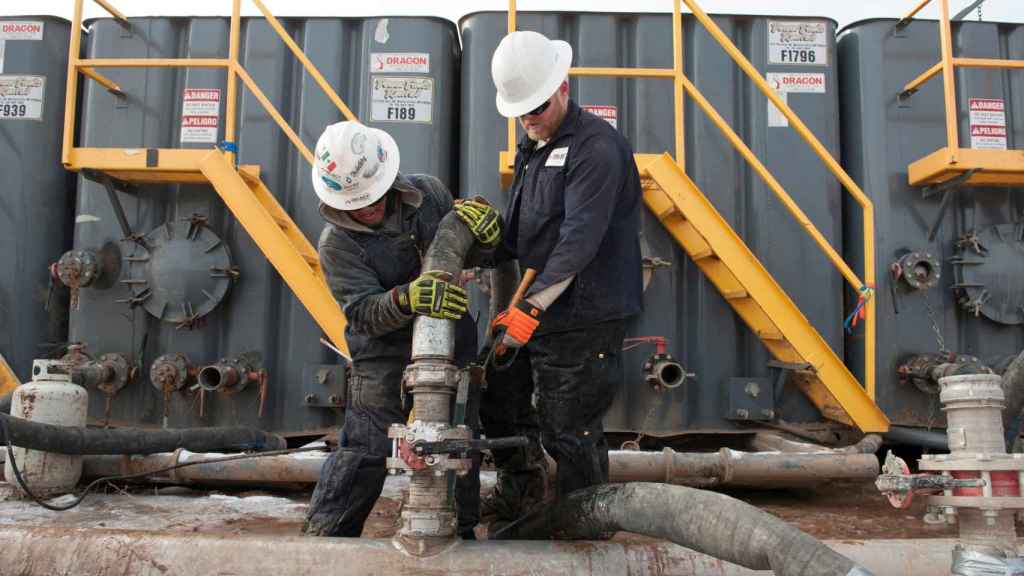 Trabajadores conectan mangueras entre una tubería y tanques de agua de fracking en Hess (EEUU).