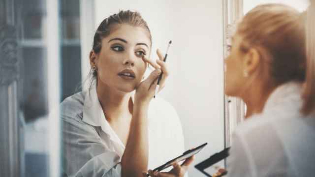 Una mujer se maquilla frente al espejo.