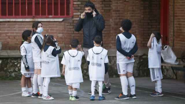Un entenador enseña a jugar al fútbol a un grupo de niños y niñas con la equipación del Real Madrid.