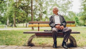 Un anciano sentado en el banco de un parque.