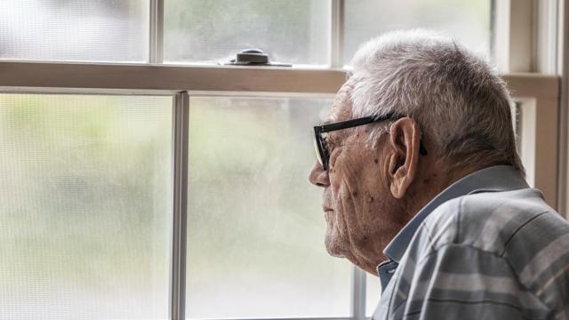 Un anciano con demencia mirando a través de la ventana.