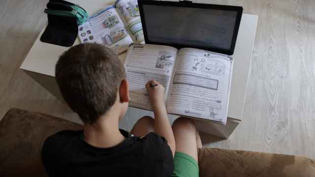 Un alumno de primaria hace los deberes con varios libros y un ordenador.