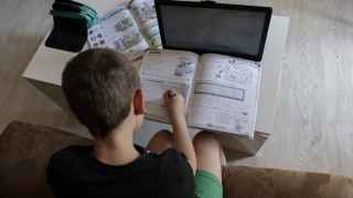 Un alumno de primaria hace los deberes con varios libros y un ordenador.