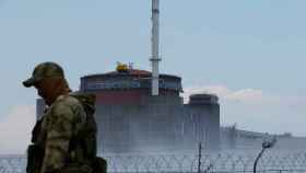 Un guarda de seguridad vigila la central nuclear de Zaporiyia con uno de sus reactores al fondo.