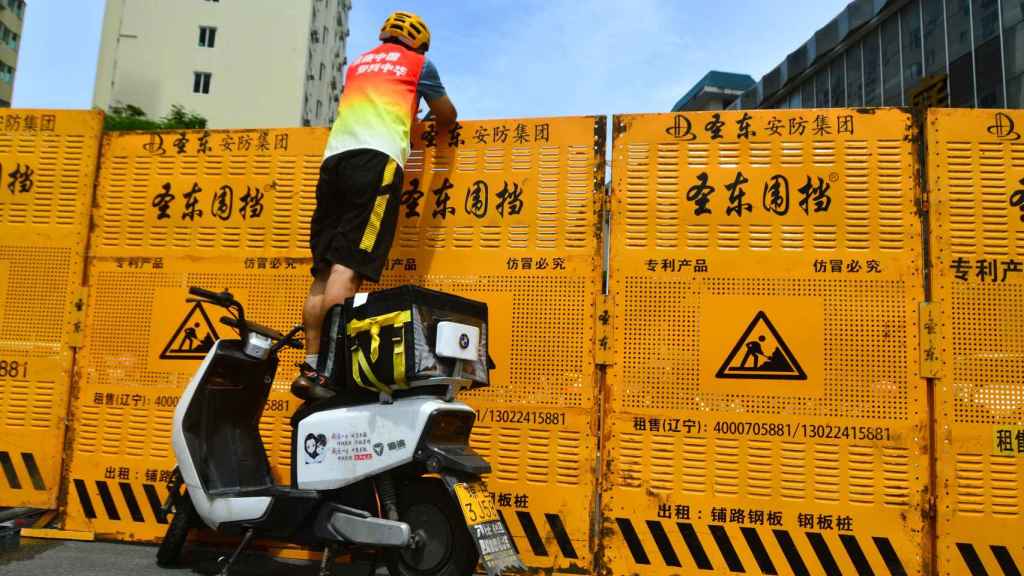 Un mensajero hace una entrega sobre una barricada en Sanya, China.