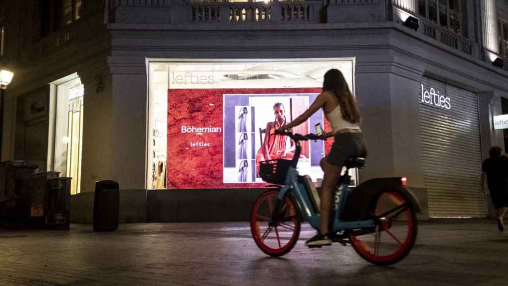 Una chica pasea con su bicicleta con los carteles iluminados de fondo.