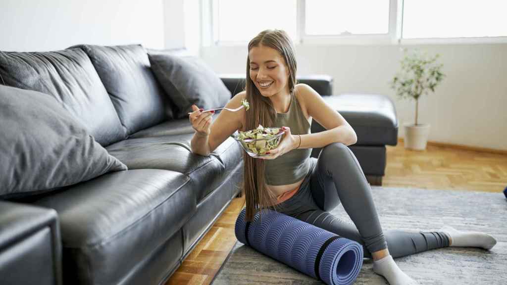 Una mujer joven come una ensalada después de haber practicado deporte.
