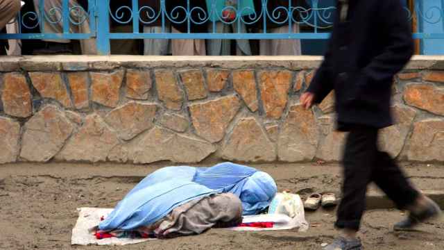 Una mujer afgana cubierta con un burka mendiga junto a su hija en la calle.