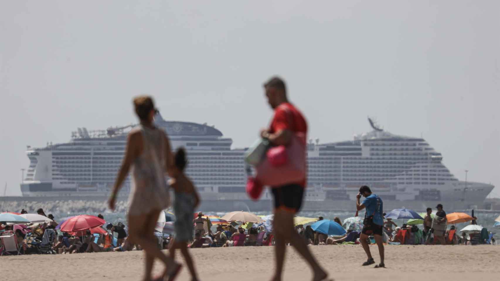 Varios turistas en una playa valenciana con varios cruceros de fondo, este verano.