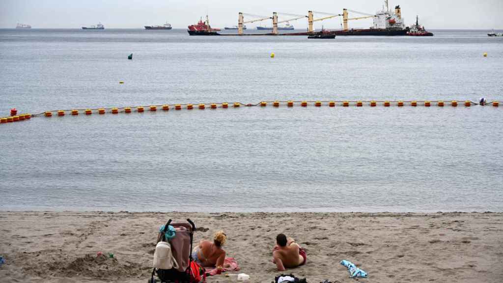 Una pareja de bañistas observa el granelero varado frente a la playa de Gibraltar.