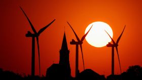 Las turbinas de molinos de viento que generan energía y la iglesia del pueblo se muestran durante la puesta de sol en un parque eólico en Bethencourt (Francia)