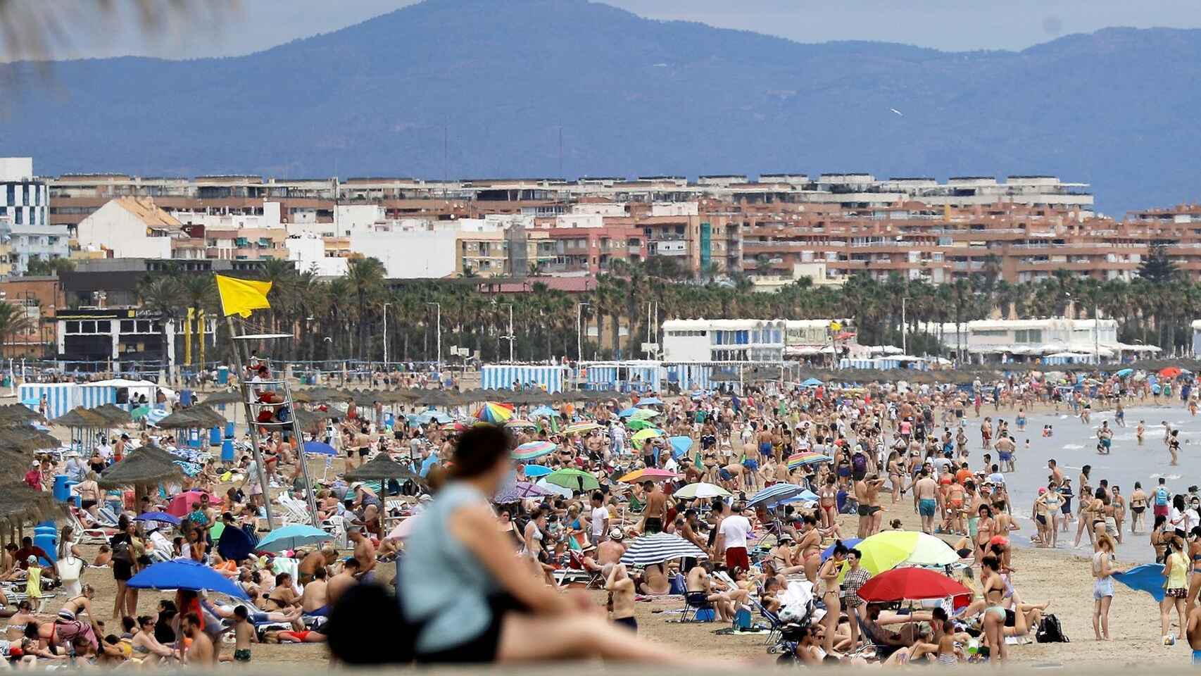 Una turista frente a una playa valenciana llena de gente, en imagen de archivo.