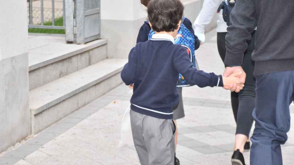 Un niño de la mano de su abuelo entra en el colegio