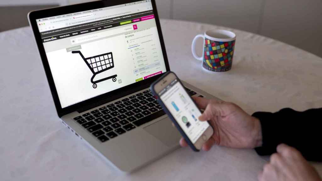 Una persona realizando compras online con su teléfono móvil y ordenador