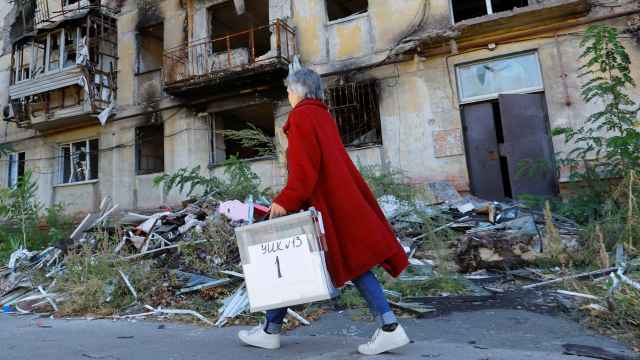 Un miembro de la comisión electoral pasa por delante de un edificio destruido con una urna portátil en Mariúpol.