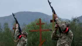 Dos soldados ucranianos homenajean a un compañero fallecido apuntando sus armas al aire.
