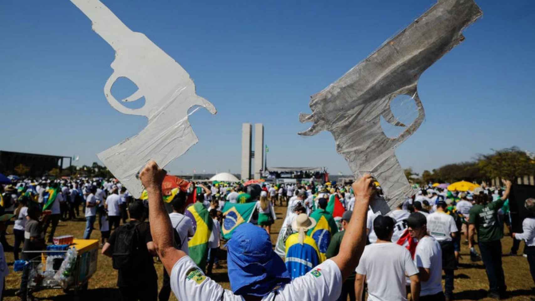 Un hombre sujeta dos armas de papel en una manifestación pro Bolsonaro.