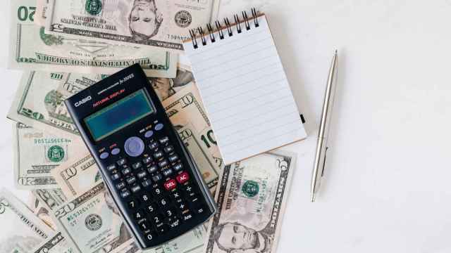 Una calculadora, un bloc de notas y un boli encima de un puñado de dólares.