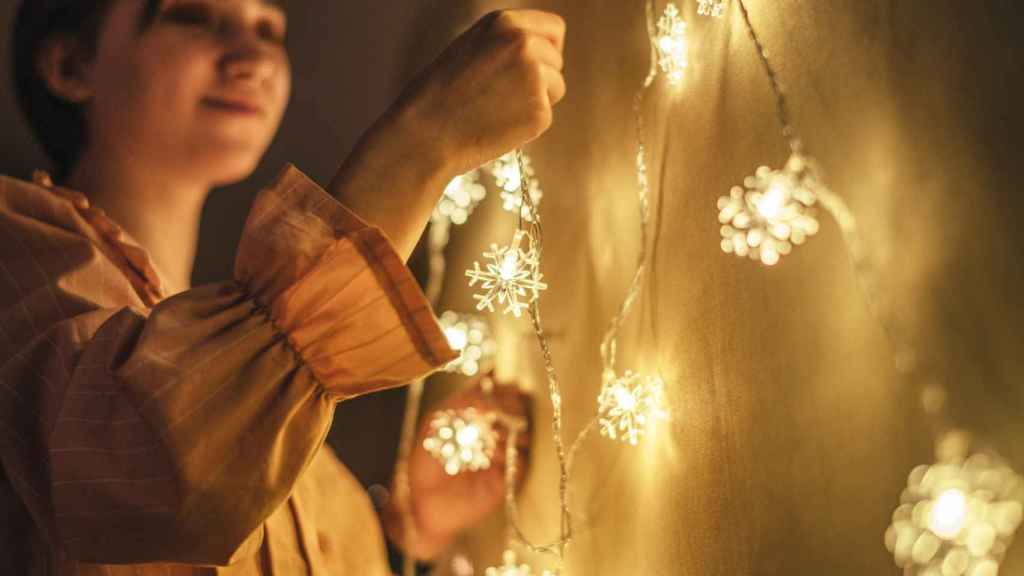 Una joven coloca luces navideñas en su dormitorio.