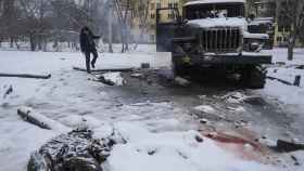 El cuerpo de un soldado cubierto de nieve mientras un hombre hace fotos de un vehículo ruso destruido en las afueras de Járkov, en una imagen del pasado febrero.