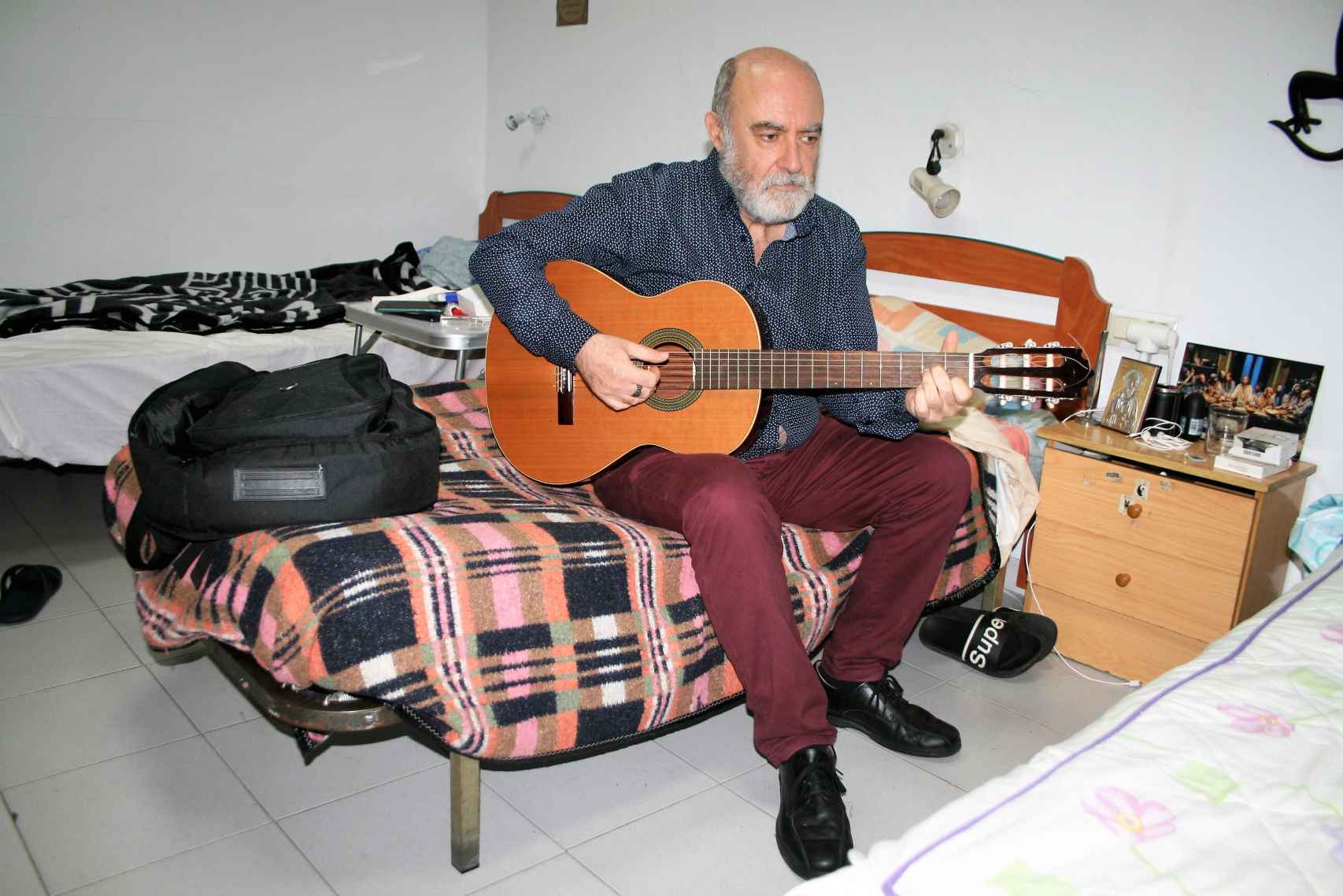 Juan Carlos Rodríguez toca la guitarra en su cama en la casa de acogida de Cristo Vive en Sevilla, en noviembre de 2022.