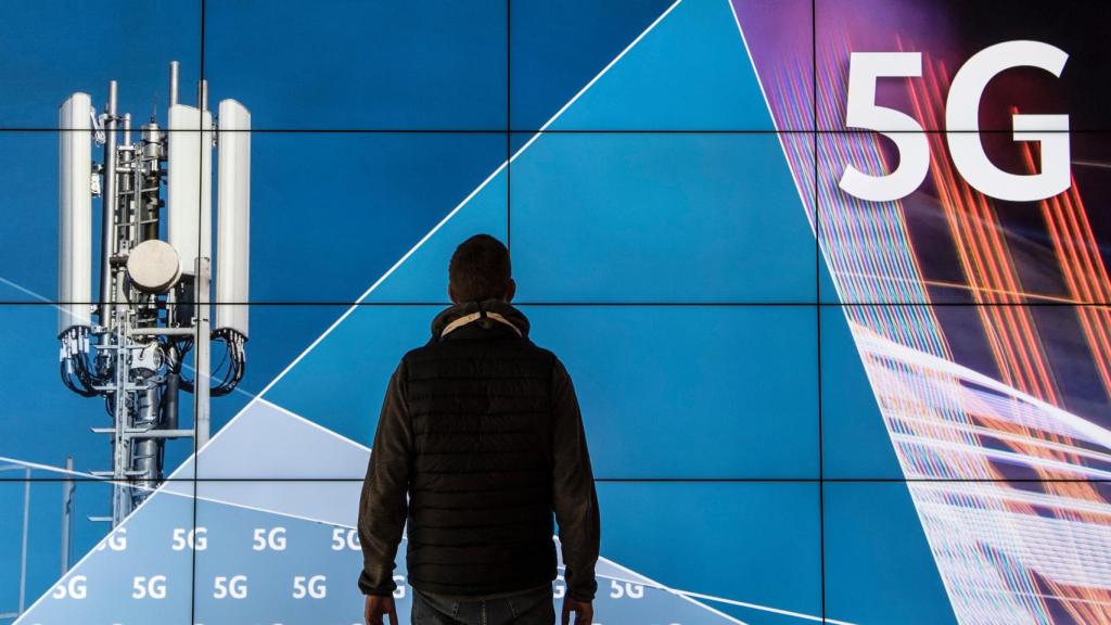 Un hombre delante de una pantalla con el logo del 5G y una antena de telecomunicaciones.