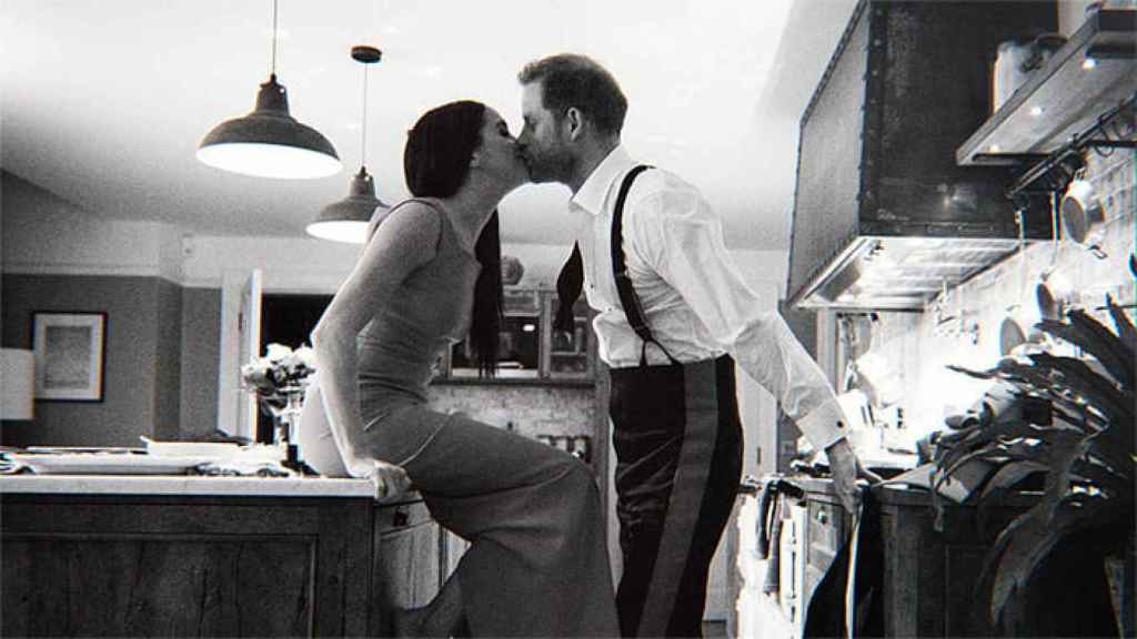 Los duques de Sussex en otra fotografía, en blanco y negro, besándose en el salón de su casa.