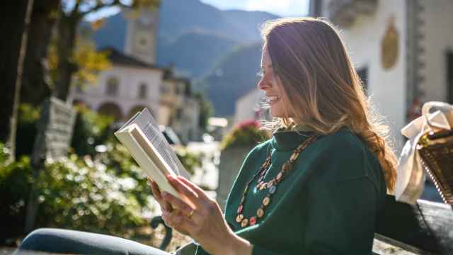 Una mujer lee un libro en una terraza de un pueblo.