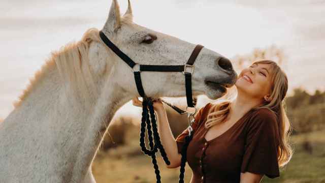 Una mujer rubia mimándose con un caballo blanco.