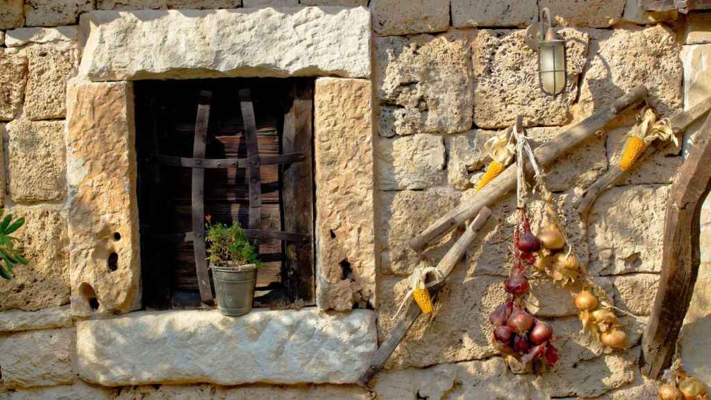 Imagen de archivo con cebollas colgando al lado de la ventana de una casa de piedra.