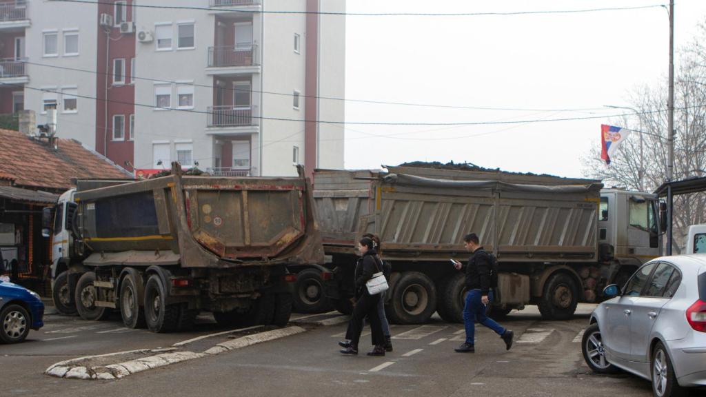 People cross a street near a road block in the northern part of the ethnically divided city of Mitrovica, Kosovo, on December 27, 2022.