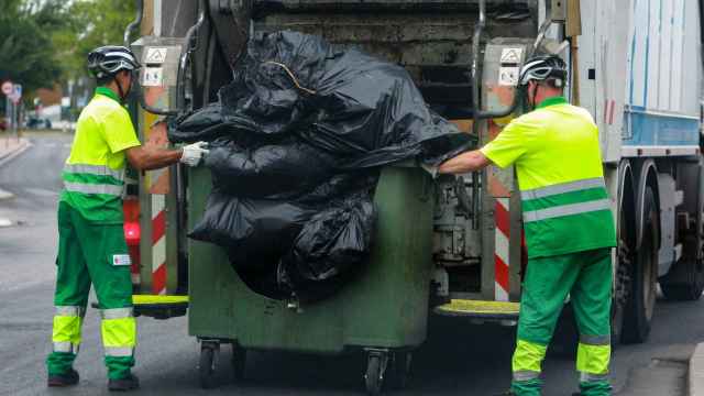 Dos trabajadores del servicio de recogida de basuras, vacían un contenedor en Madrid.
