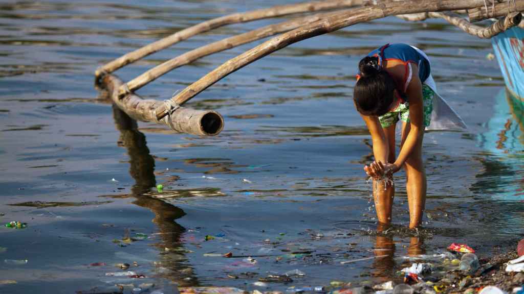 Una mujer se lava las manos en un río contaminado de Filipinas.