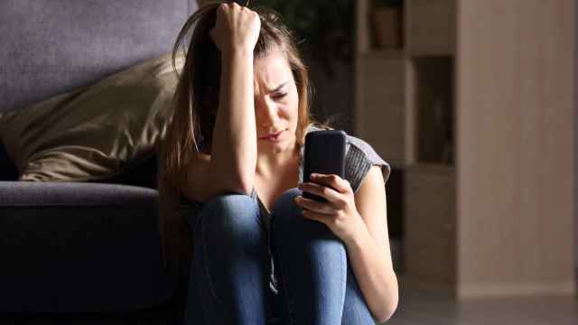 Una joven mira su teléfono llorando.